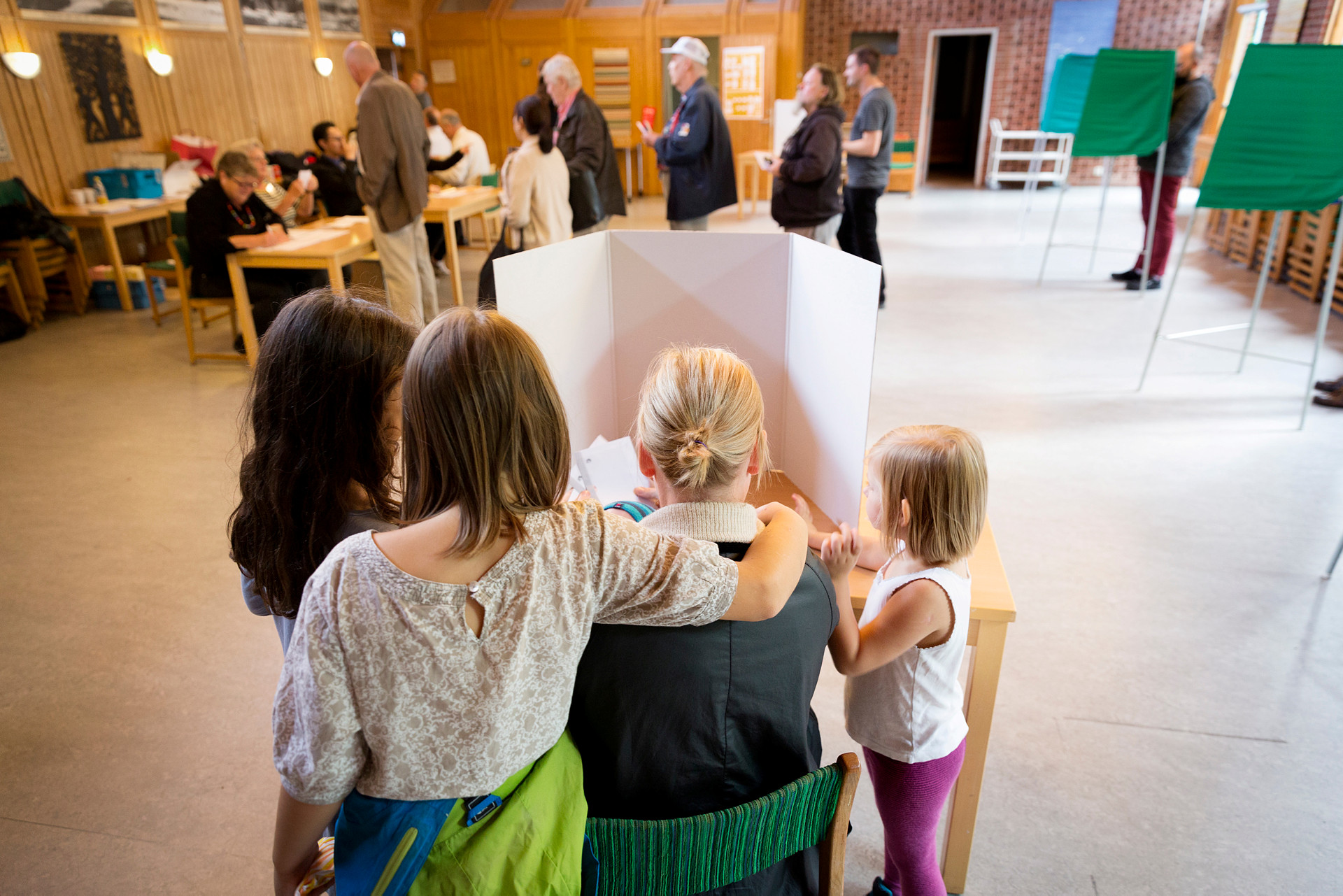 Röstande i en vallokal 2017. En mamma röstar i valbåset omgiven av tre barn.