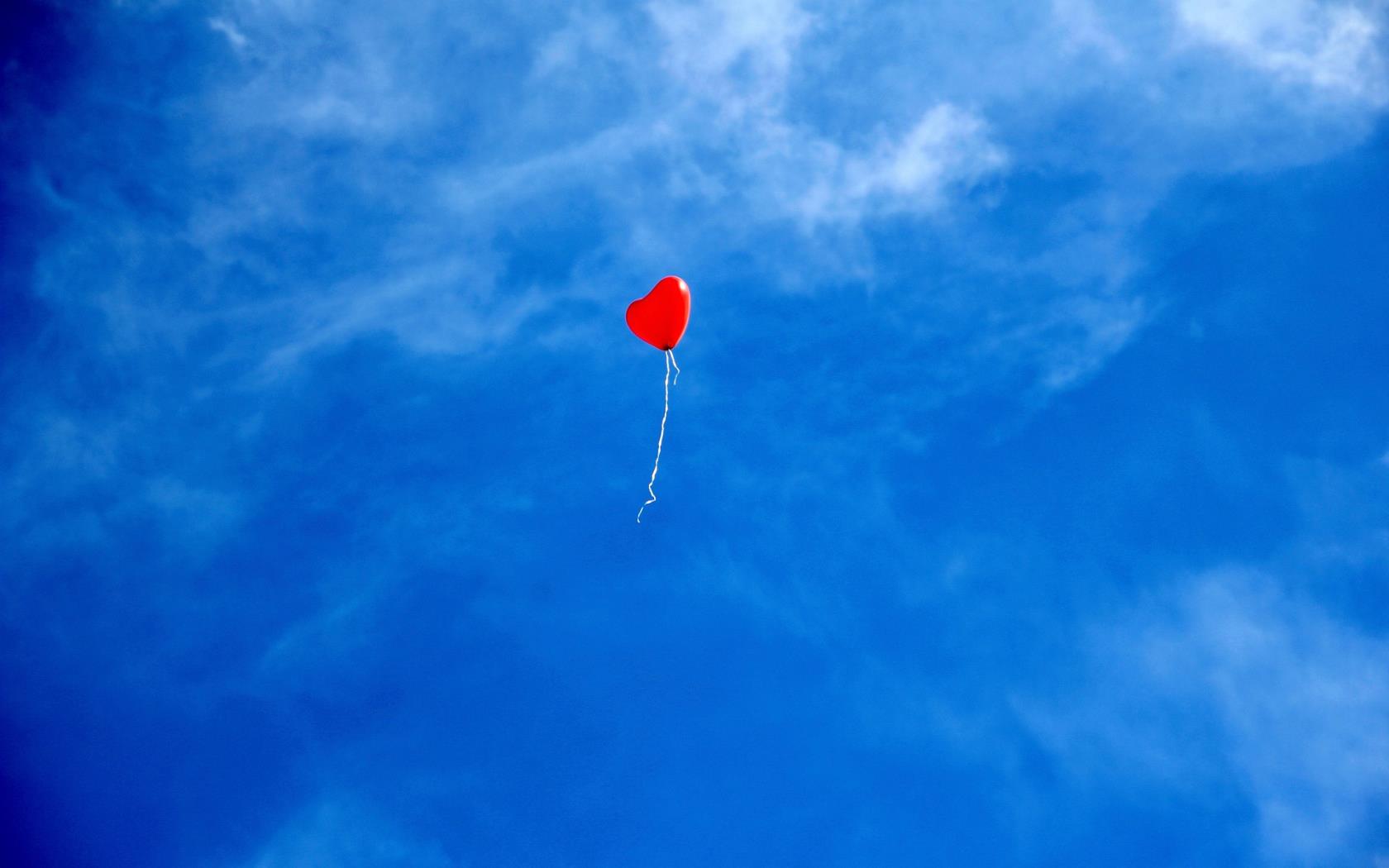 Hjärtformad röd ballong mot blå himmel