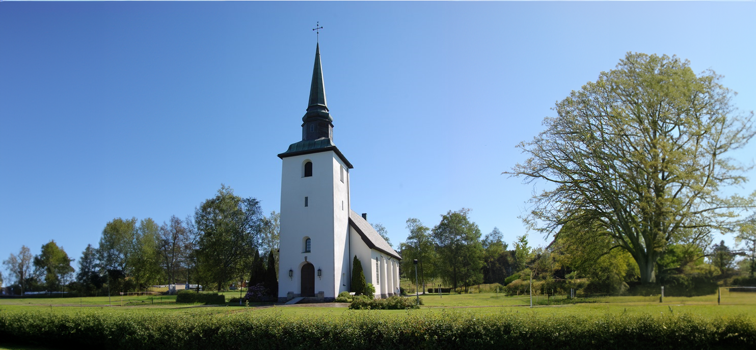 Blomskogs vita kyrka med grönskande kyrkogård.