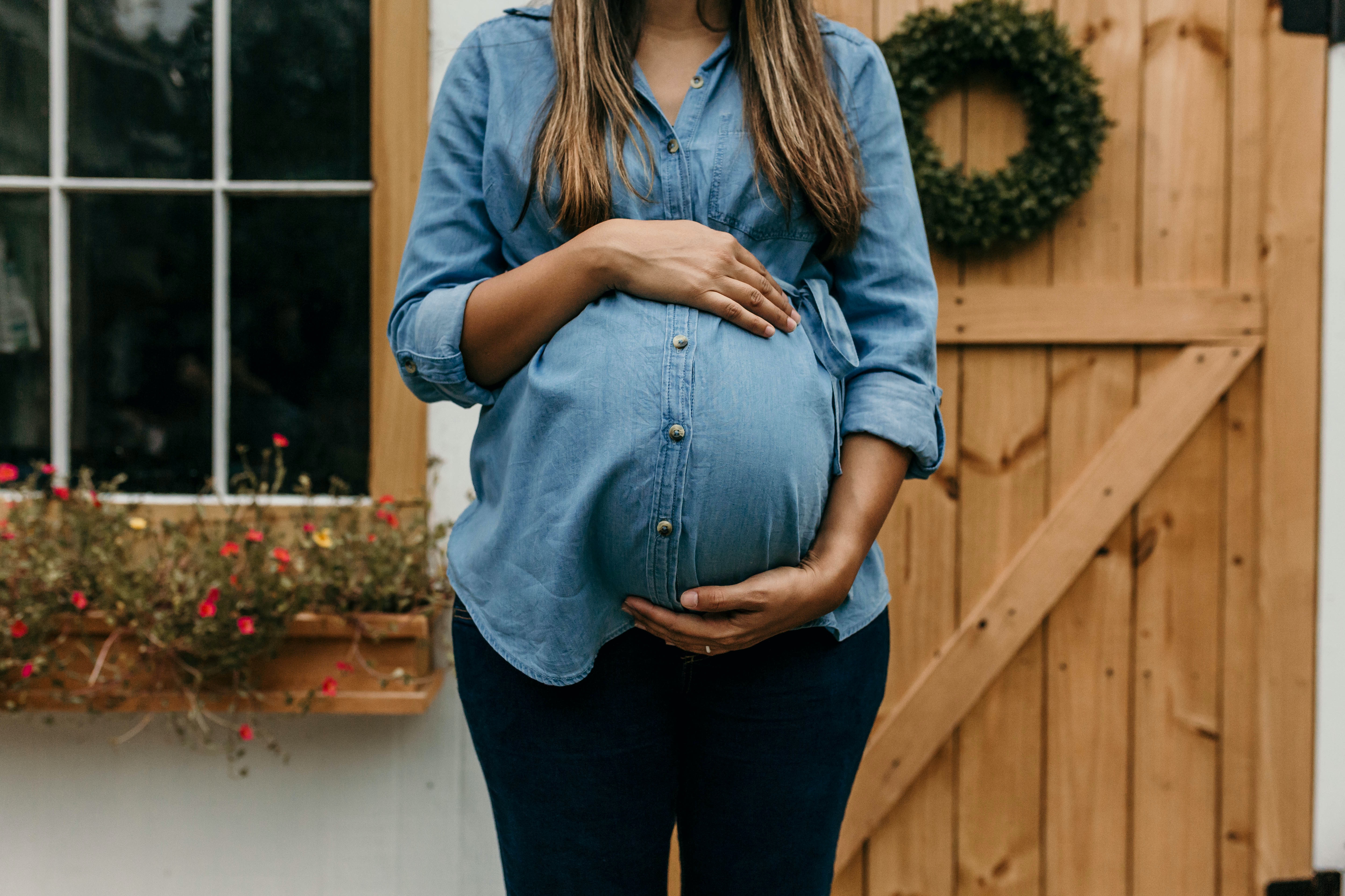 Gravid kvinna i blå skjorta håller händerna runt den runda magen