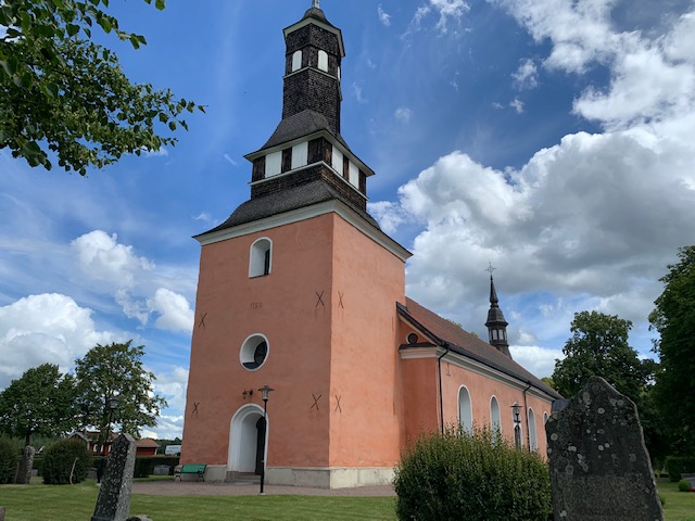 Ekeby kyrka, en rosa kyrka med tornet och ingången.