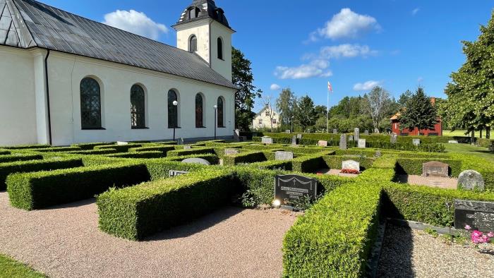 Rinna kyrkogård med kyrkan i bakgrunden. Framför kyrkan finns gravar med välklippta häckar.