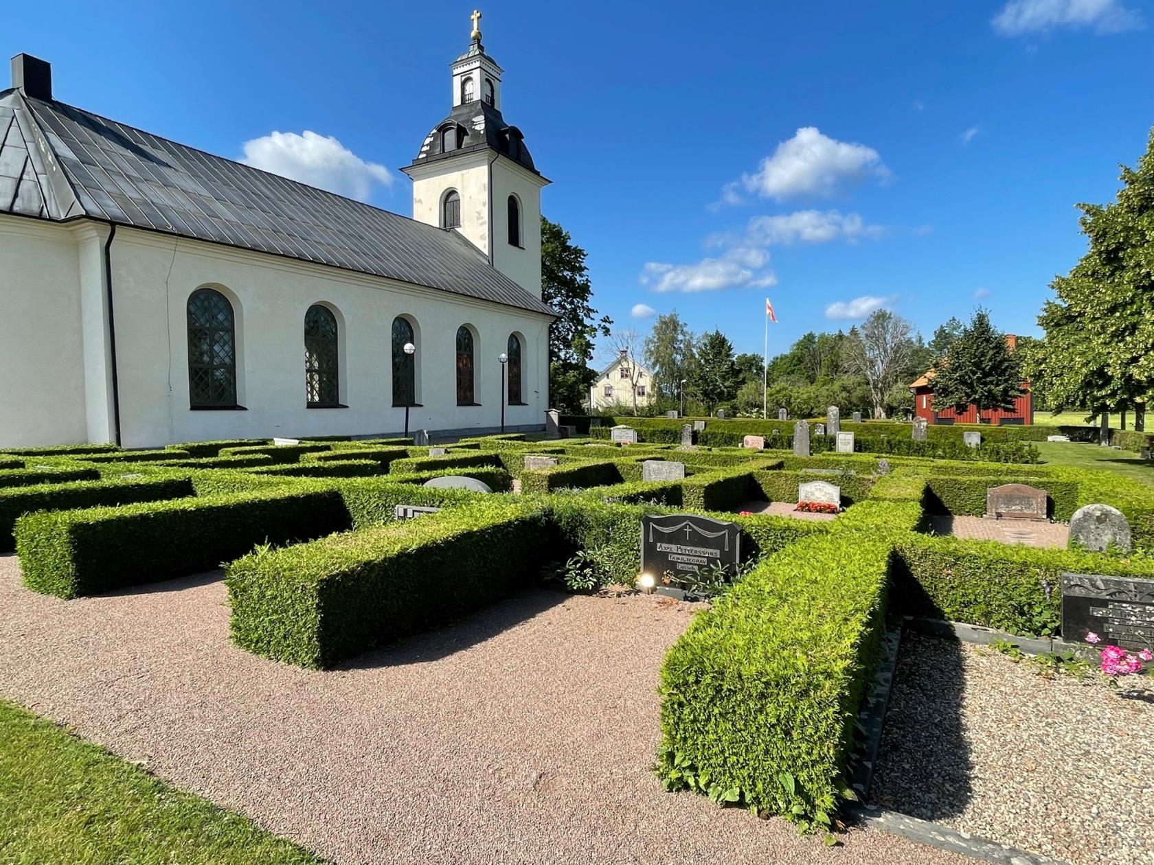 Rinna kyrkogård med kyrkan i bakgrunden. Framför kyrkan finns gravar med välklippta häckar.