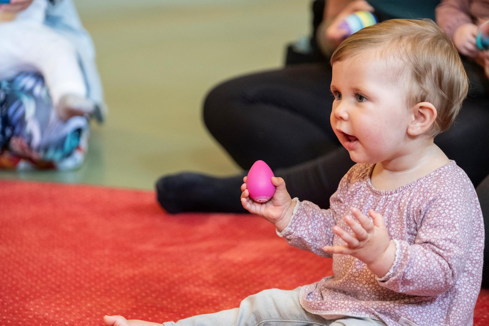 Barn på babyrytmik med en äggskallra i handen.