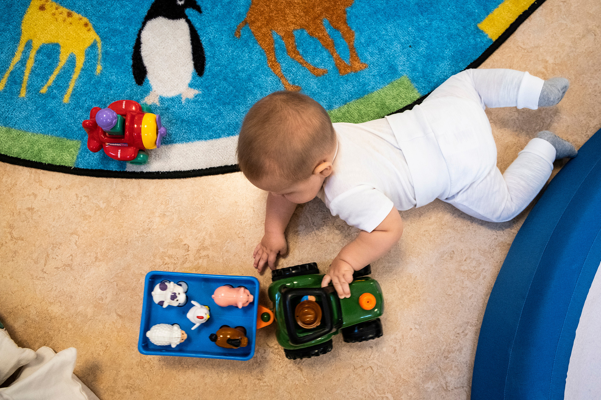 Bilden föreställer en bebis på golvet som leker med en traktor med släp. 