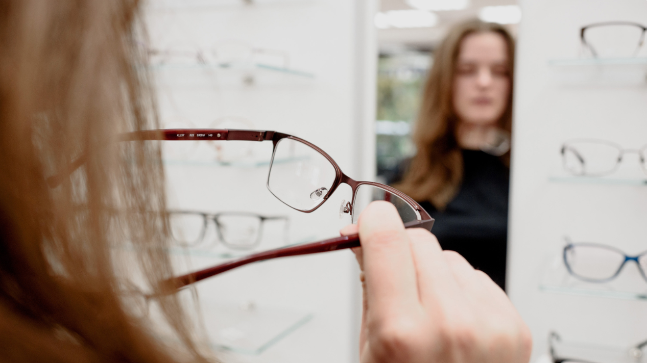 En ung tjej kollar in och testar olika bågar på glasögon i en spegel.
