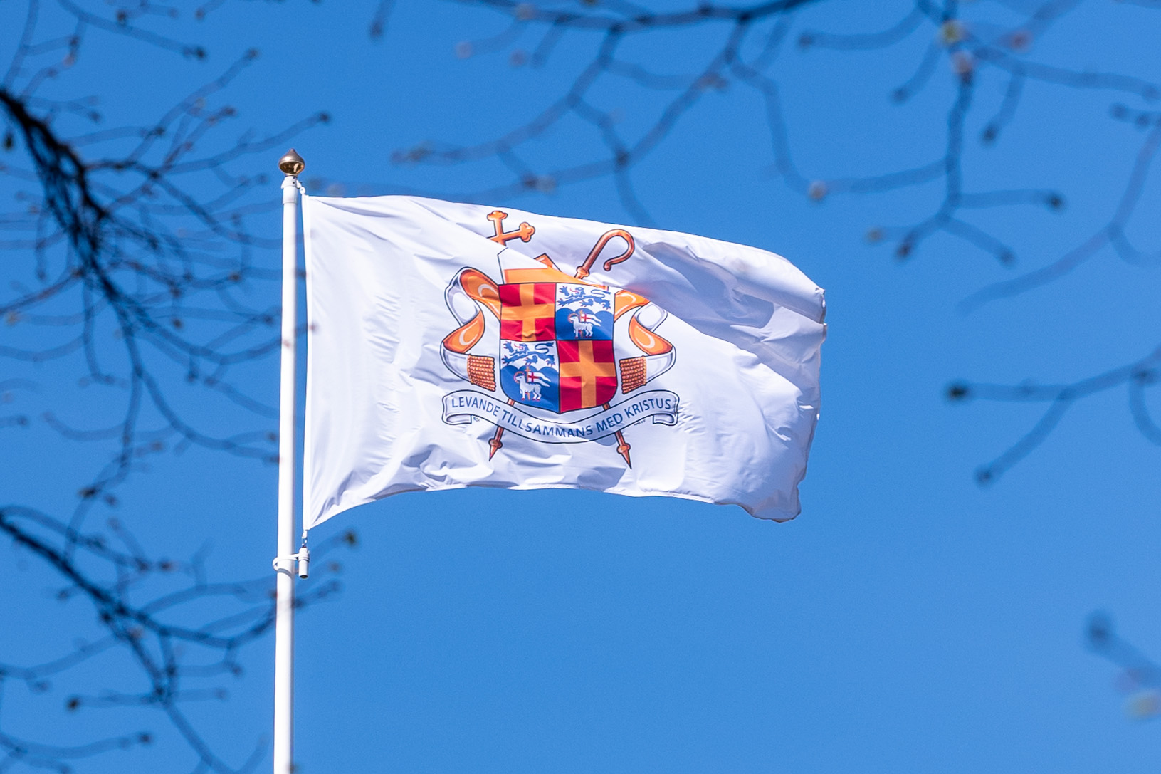 En vit flagga med ärkebiskopens vapensköld mot blå himmel.