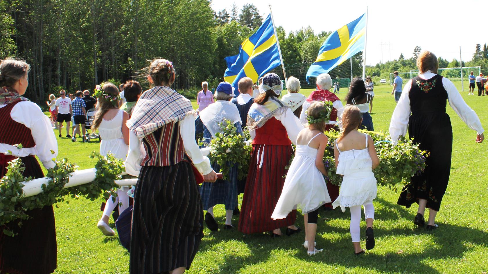 Kansallispukuiset naiset kantavat juhannussalkoa.