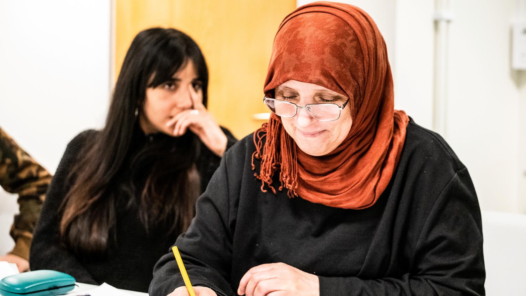 Två kvinnor som deltar på språkundervisningen sitter vid ett bord och skriver.