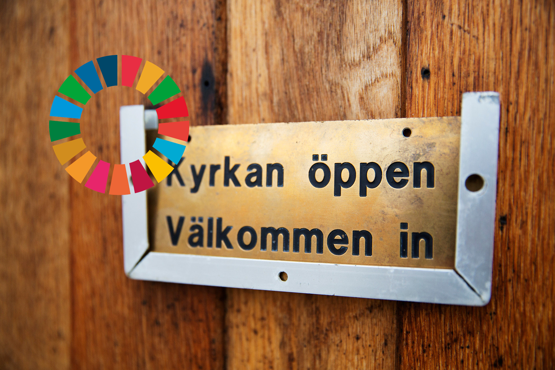 På en dörr sitter en skylt med texten Kyrkan öppen välkommen in. Till vänster syns loggan för Agenda 2030.