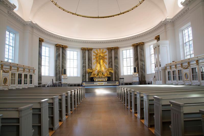 Mittgång i kyrka leder fram till altare. På båda sidorna marmoreringsmålade kyrkbänkar.