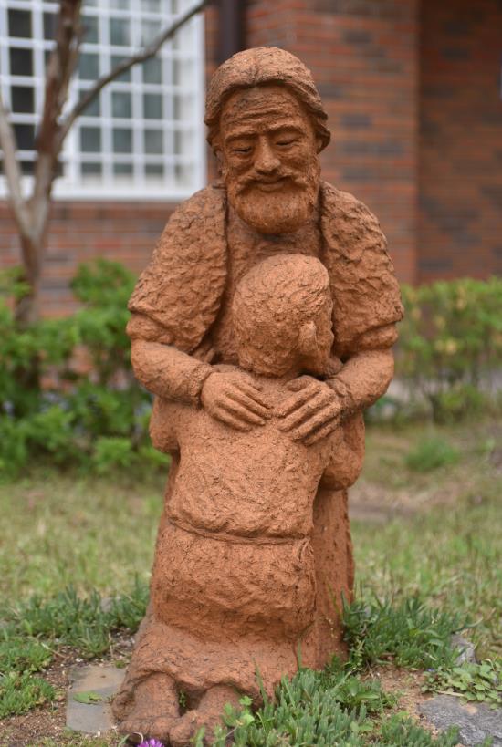 Skulptur som föreställer en leende far som håller om sin knäböjande son.