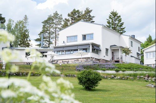 Ett stort vitt hus på en grön gräsmatta med buskar. 