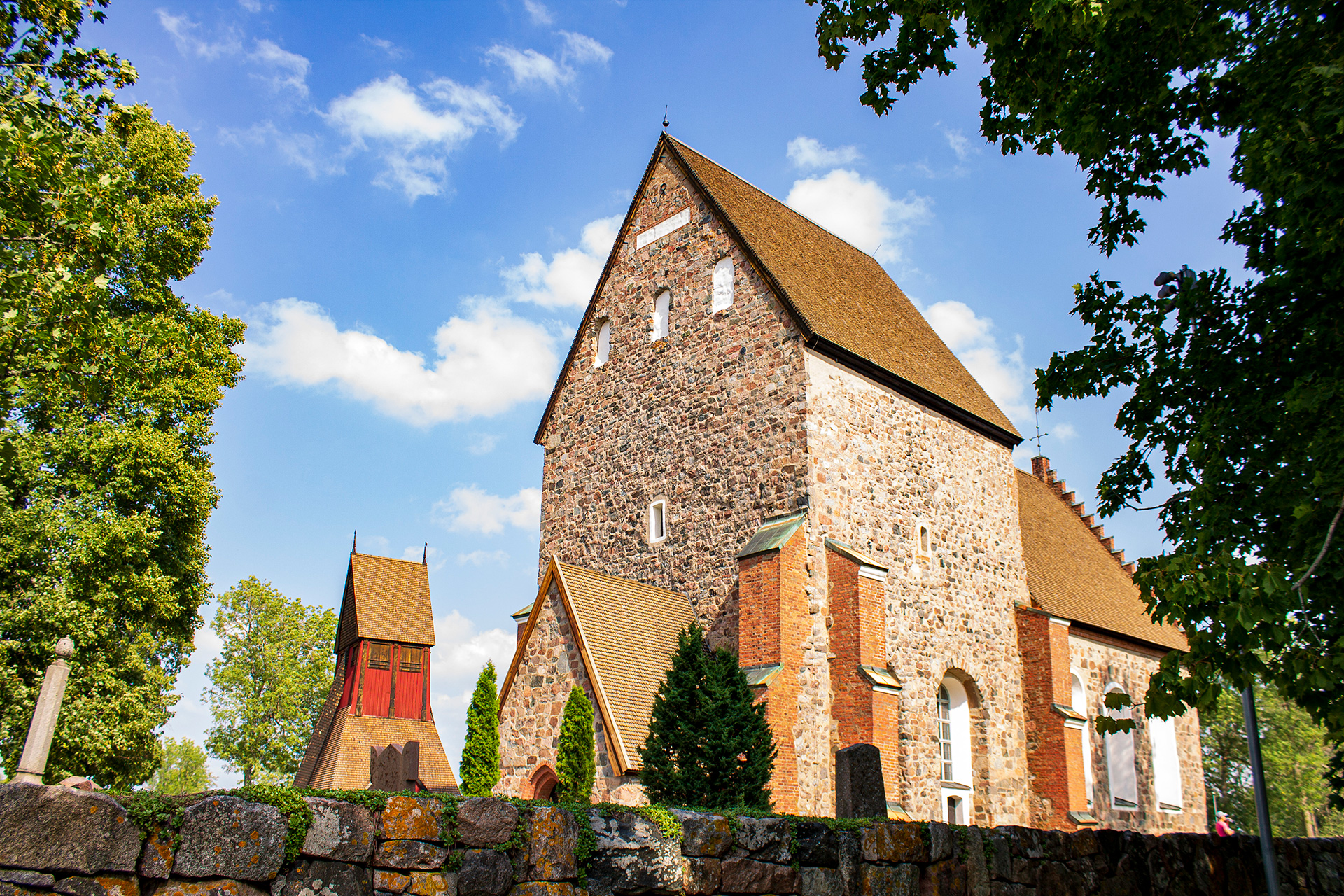 Gamla Uppsala kyrka med tillhörande stenmur en solig sommardag