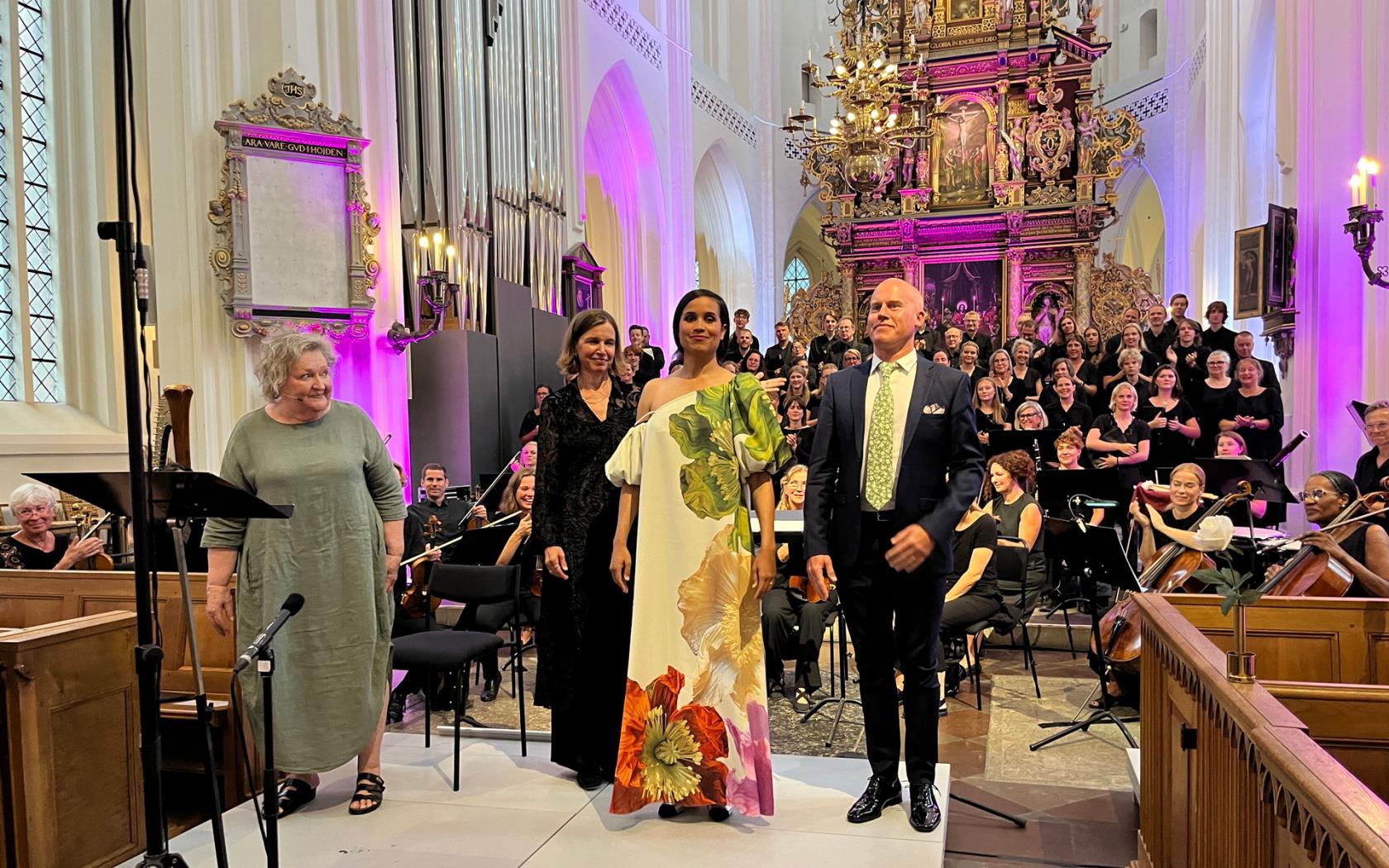 Applådtack med tre kvinnor och en man framför kör och orkester.