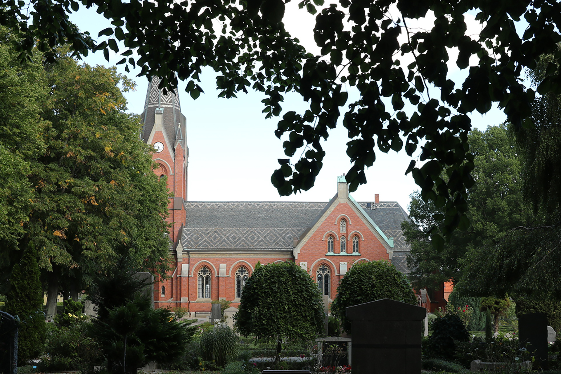Limhamns kyrka sedd från kyrkogården med träd och buskar i förgrunden.