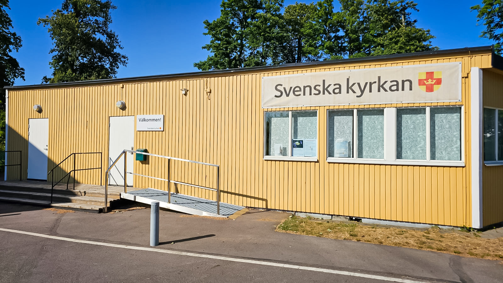 En gul byggnad med en baderoll på väggen som visar Svenska kyrkans logotyp