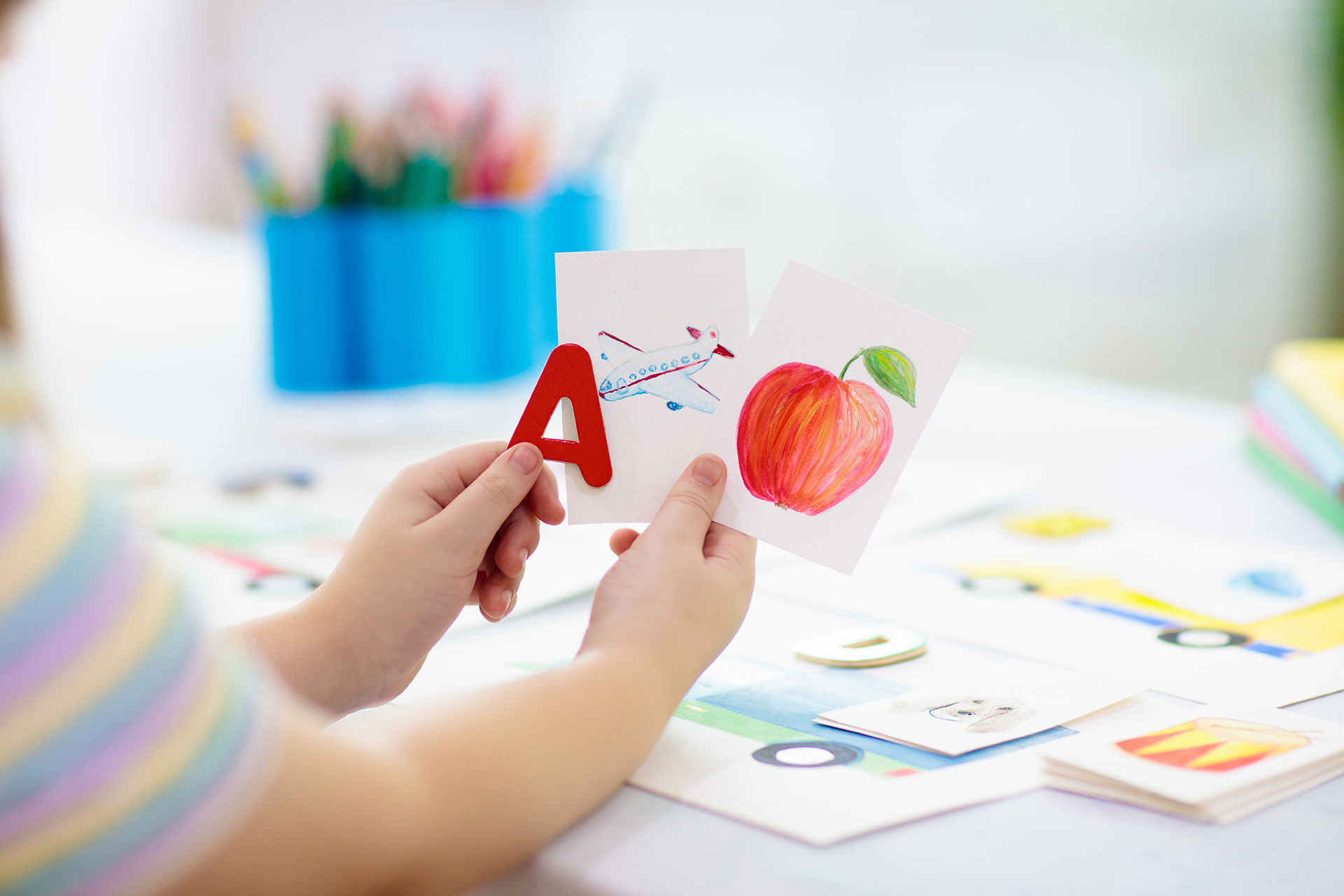 barn håller bild av äpple och bokstaven A i händerna vid ett bord med pennor och ritpapper