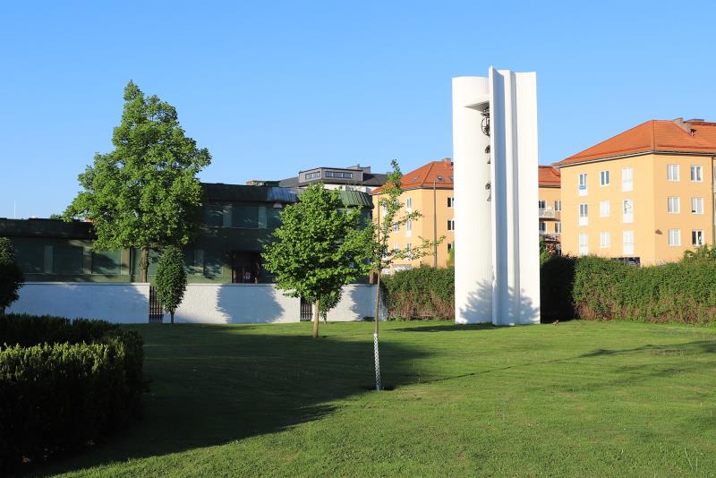 En vit klockstapel står i ett av hörnen i Matteusparken. I klockstapeln hänger tre kyrkklockor.