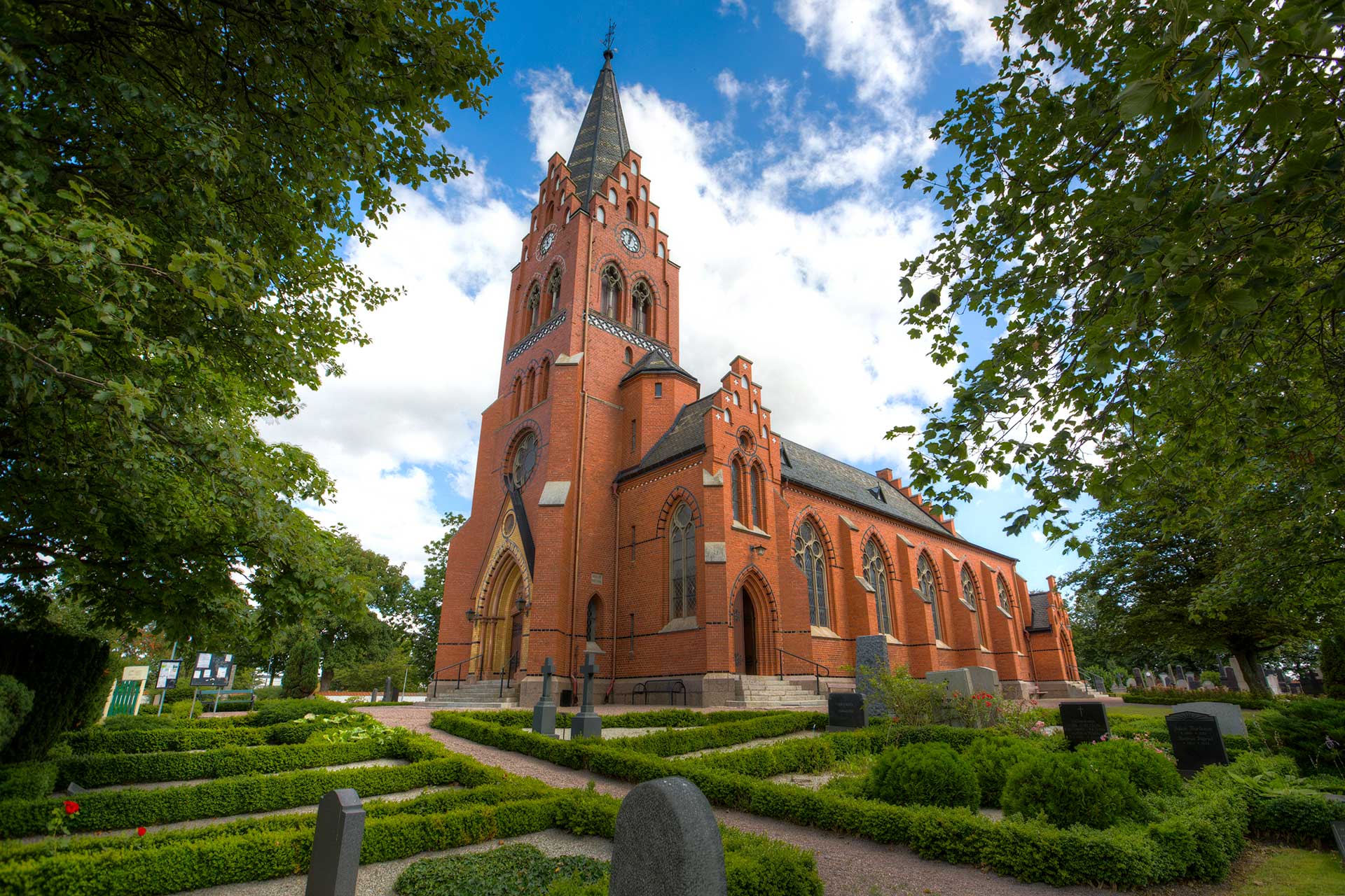 Röd tegelkyrka omgiven av träd.