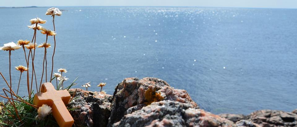 Vacker sommarvy av havet med ett kors samt blommor i förgrunden