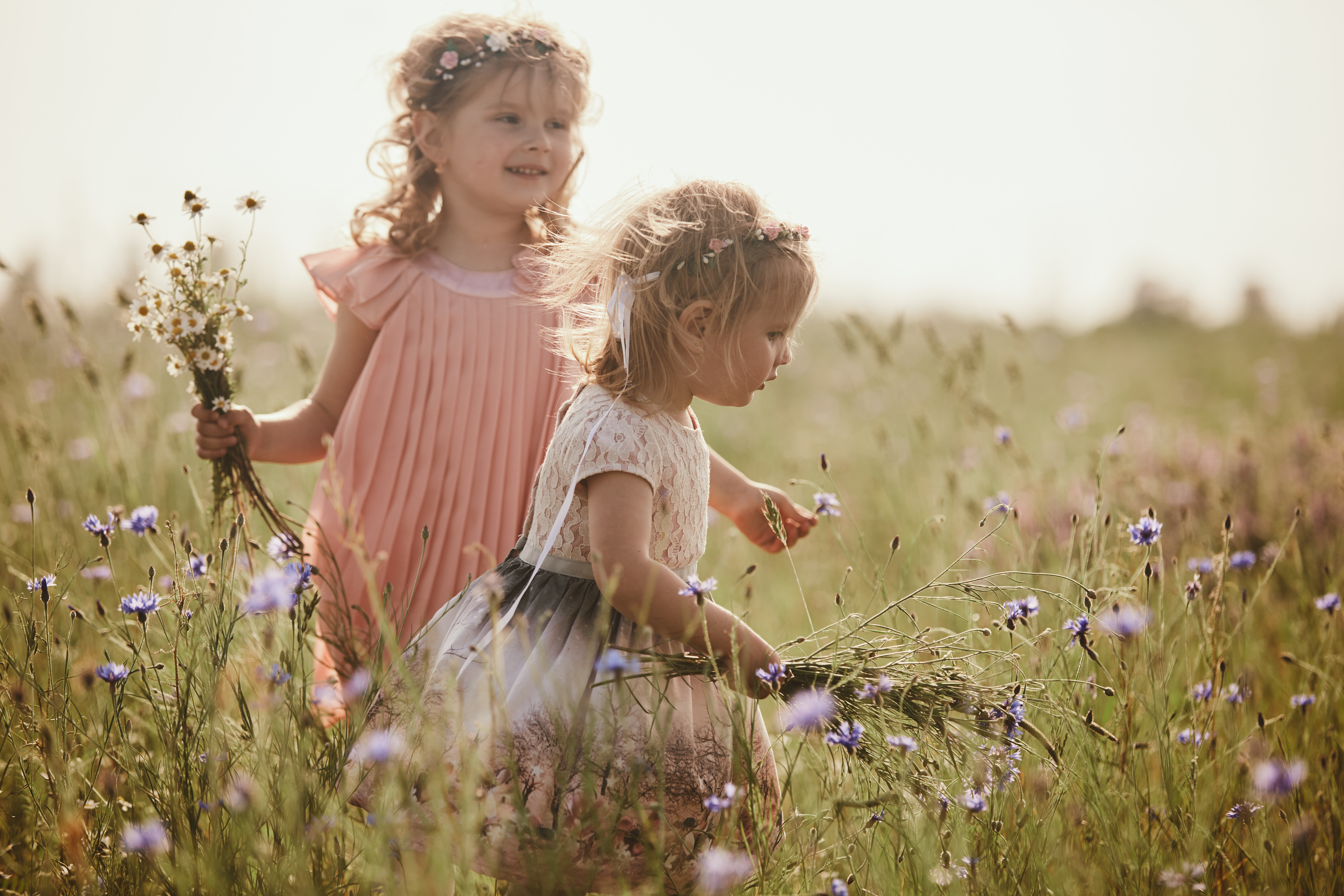 Två flickor springer genom högt gräs och blommor en sommarkväll