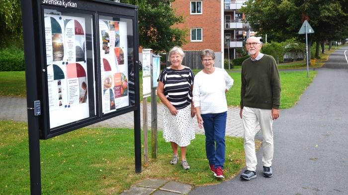 Två kvinnor och en man promenerar förbi en skylt med Svenska kyrkan