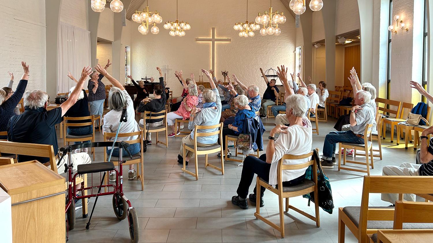 Sittgympa i Näsets kyrksal. Person sitter på stolar i en halvcirkel och sträcker på armarna. 