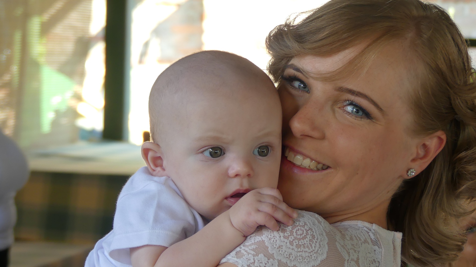 En kvinna håller en bebis nära sitt eget ansikte, bebisen ser nyfiken ut, kvinnan verkar lycklig. 