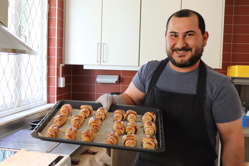 En man håller en plåt med nybakade kanelgifflar.