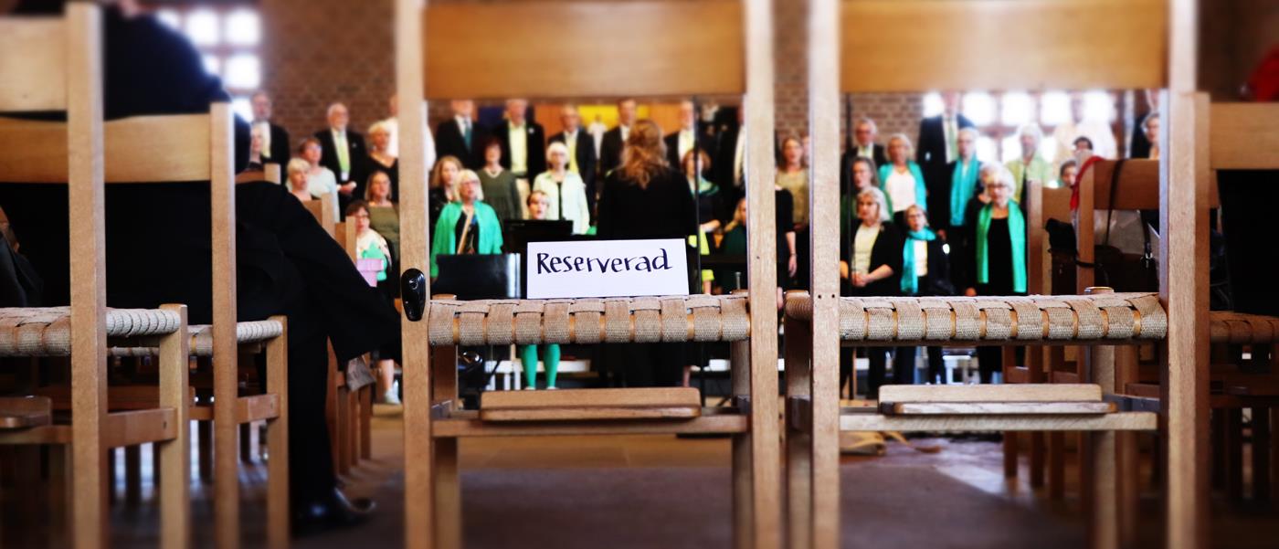 Två stolar, på den ena står ordet "reserverad", genom stolarna syns en kör som håller konsert.