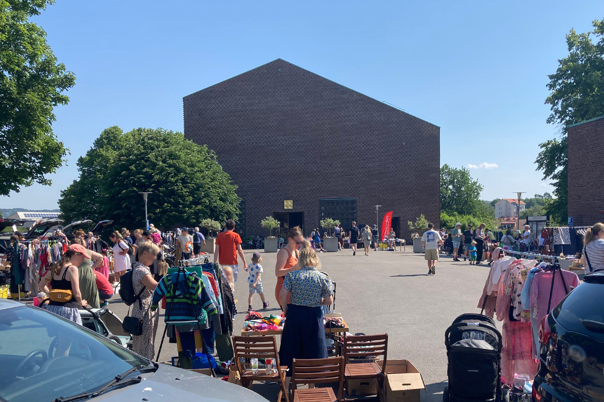 Uppställda bilar, loppisvaror och människor som rör sig framför en tegelkyrka.