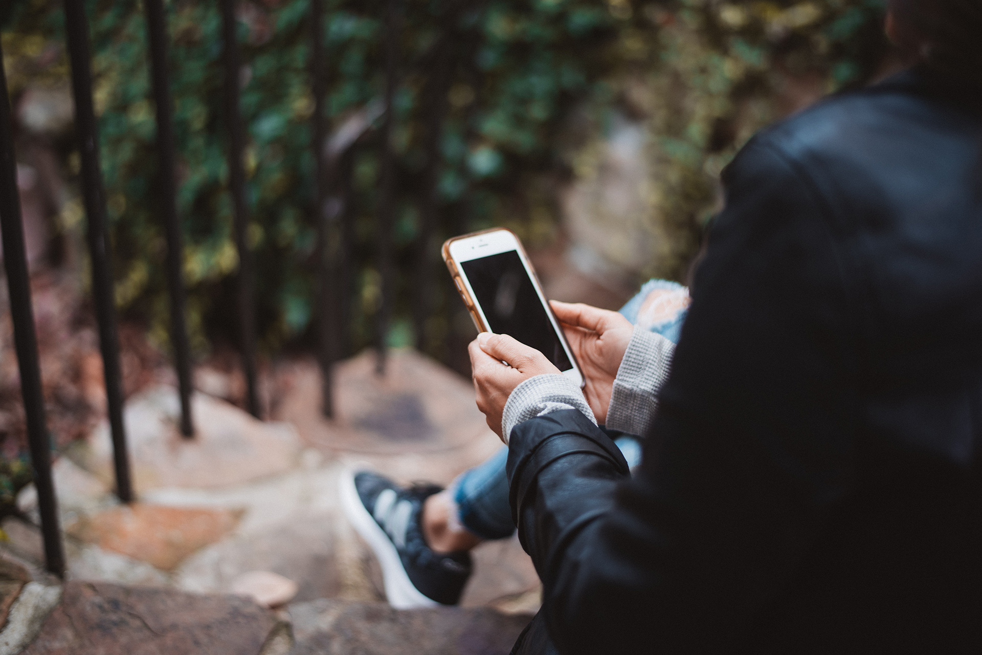 En person sitter ute på en trappa och håller en mobiltelefon.