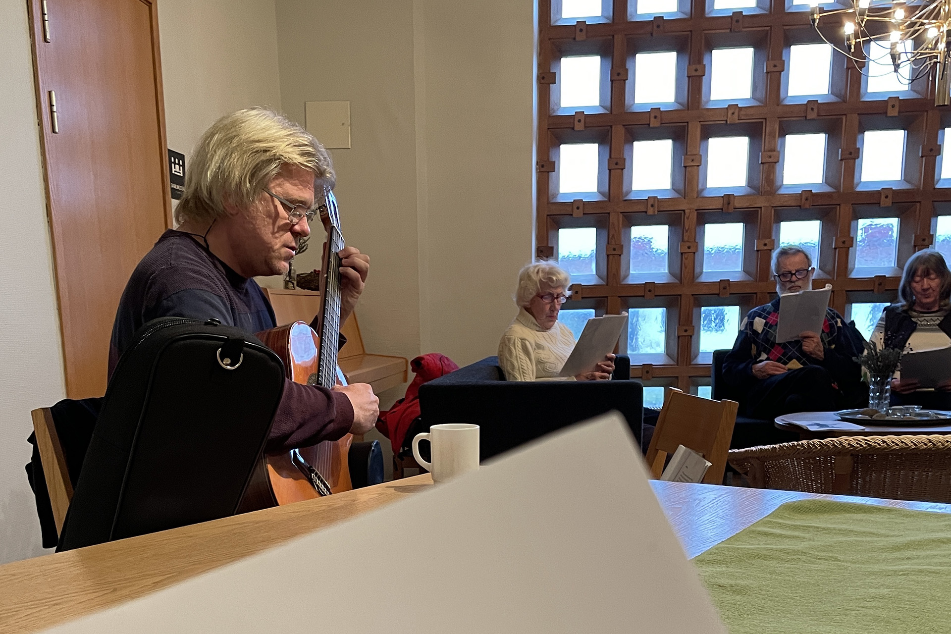 En man spelar gitarr och i bakgrunden syns deltagare som sjunger.