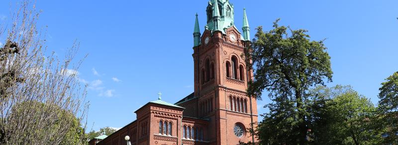 En tegelkyrka omgiven av grönska och blå himmel.