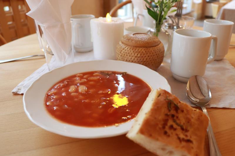 En tallrik röd tomatsoppa och hembakat bröd på ett dukat bord.