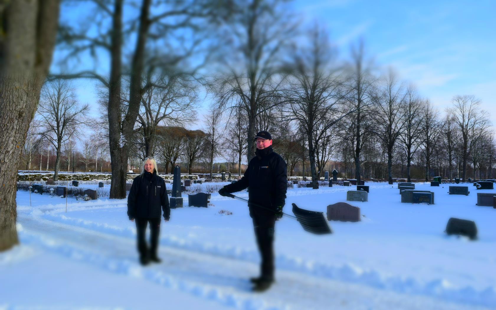 Två kyrkogårdarbetare som arbetar utomhus på snöig kyrkogård.