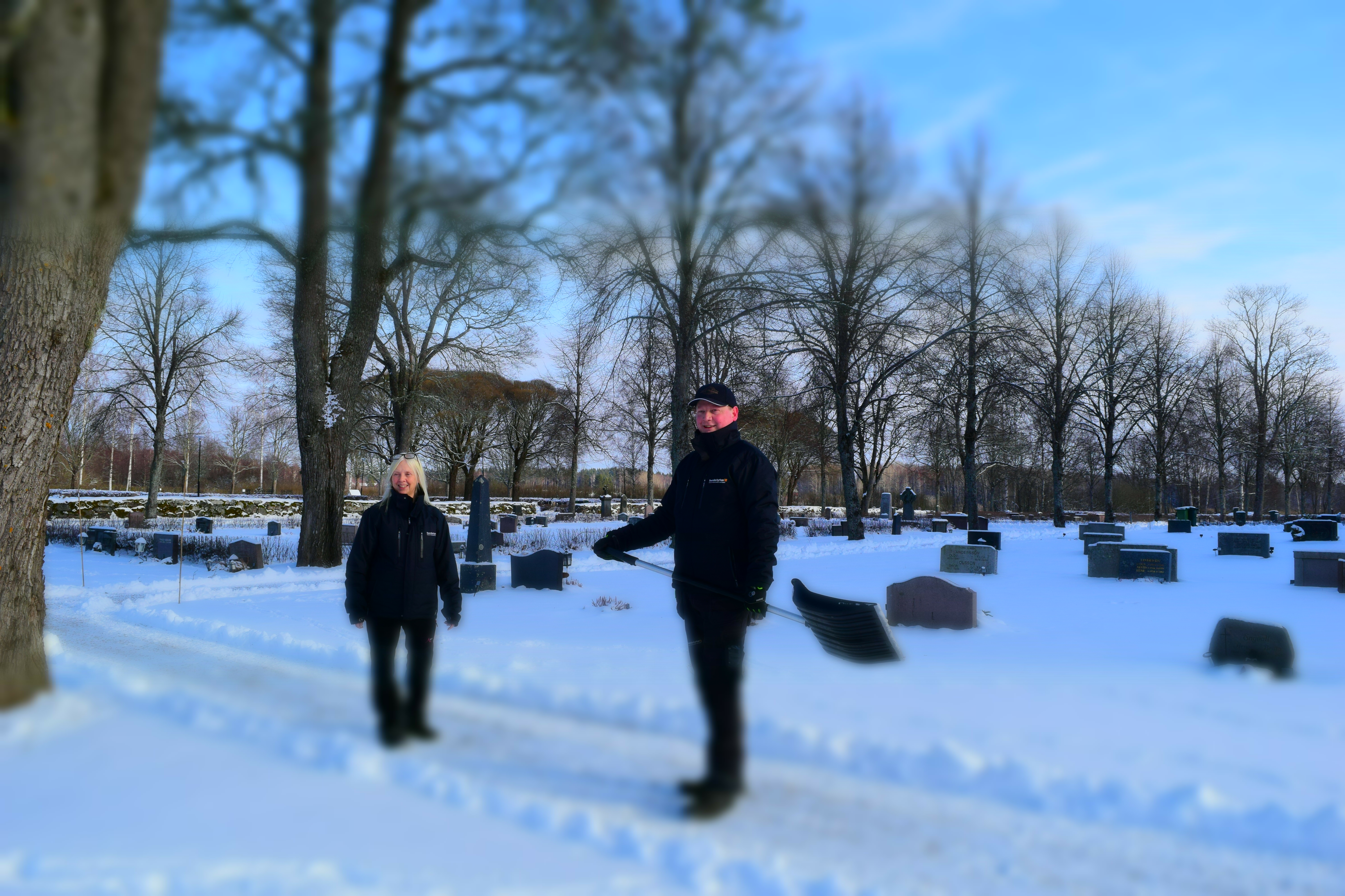 Två kyrkogårdarbetare som arbetar utomhus på snöig kyrkogård.