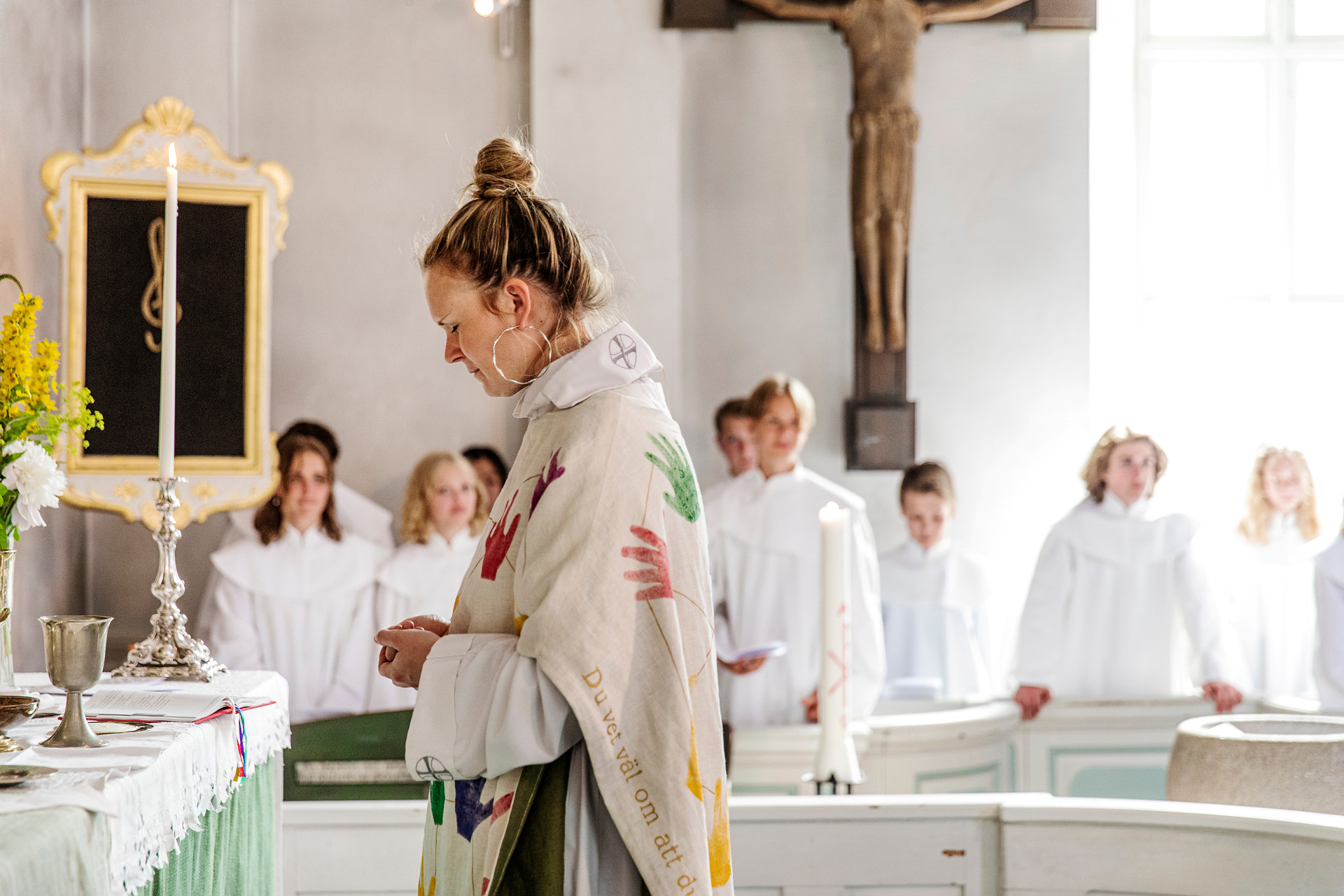 Präst vid nattvardsaltare med konfirmander i bakgrunden