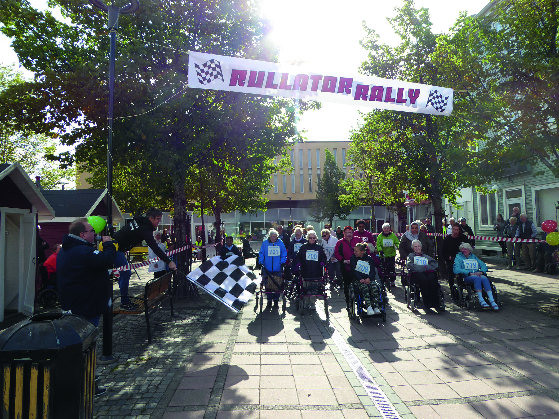 Startflagg viftas för RullatorRallyt 2019 vid start och målfållan på Kramfors torg med glada rullstolsburna deltagare i första led