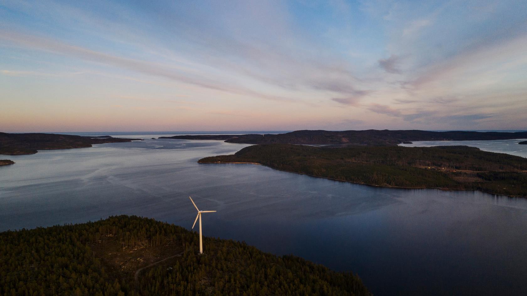 Flygfoto över kust med vidsträckt vatten och ett vindkraftverk på marken.