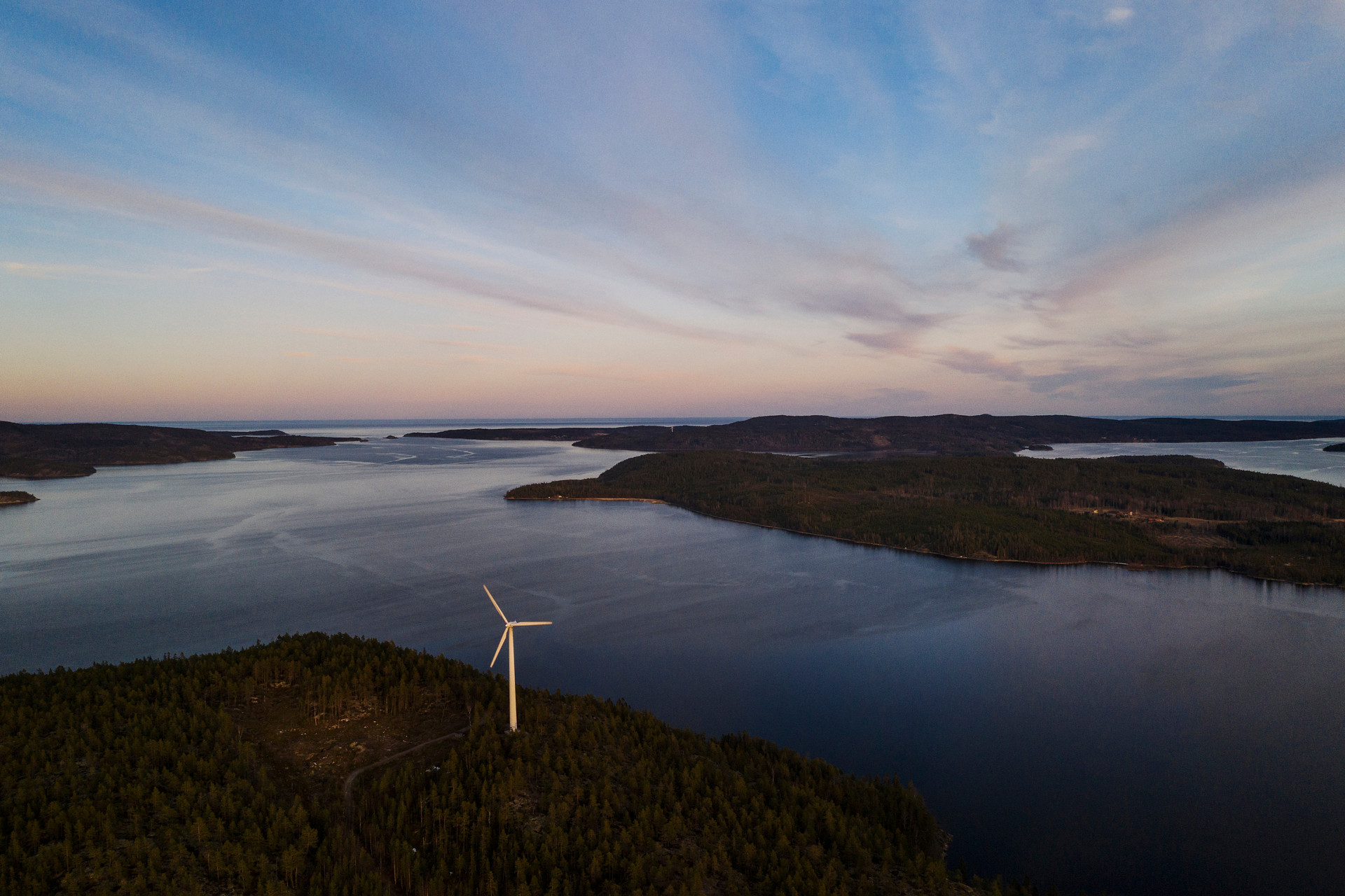 Flygfoto över kust med vidsträckt vatten och ett vindkraftverk på marken.