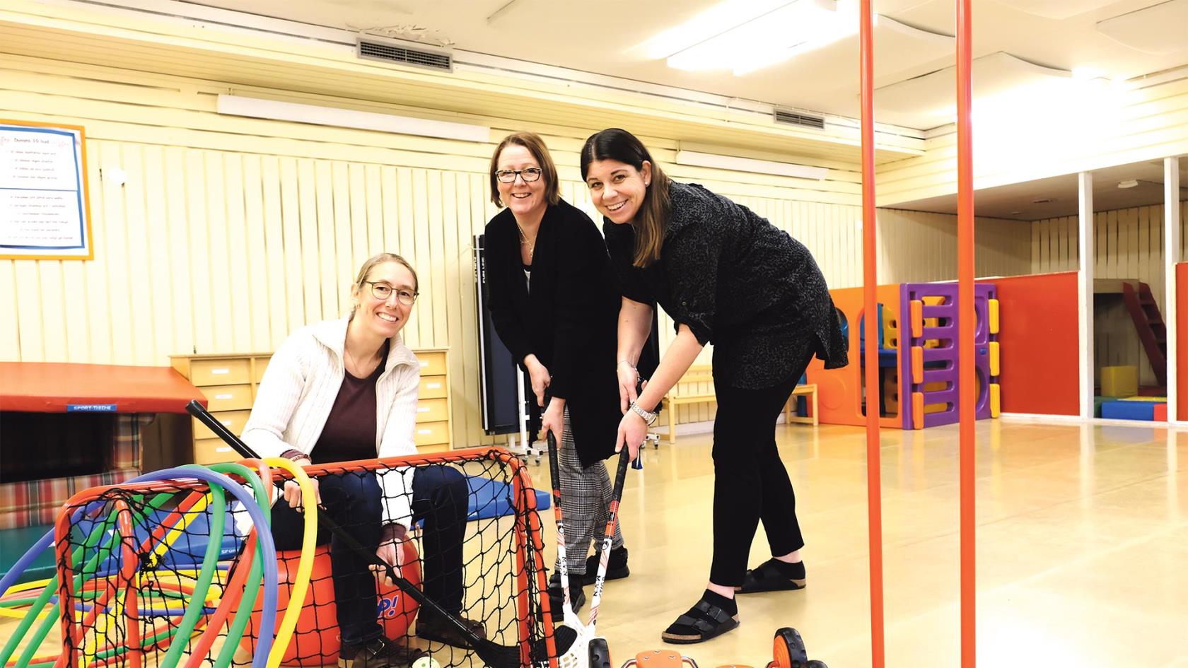 Tre pedagoger på Duvan i en leksal inomhus. Ett innebandymål i förgrunden. Alla håller en innebandyklubba i handen.