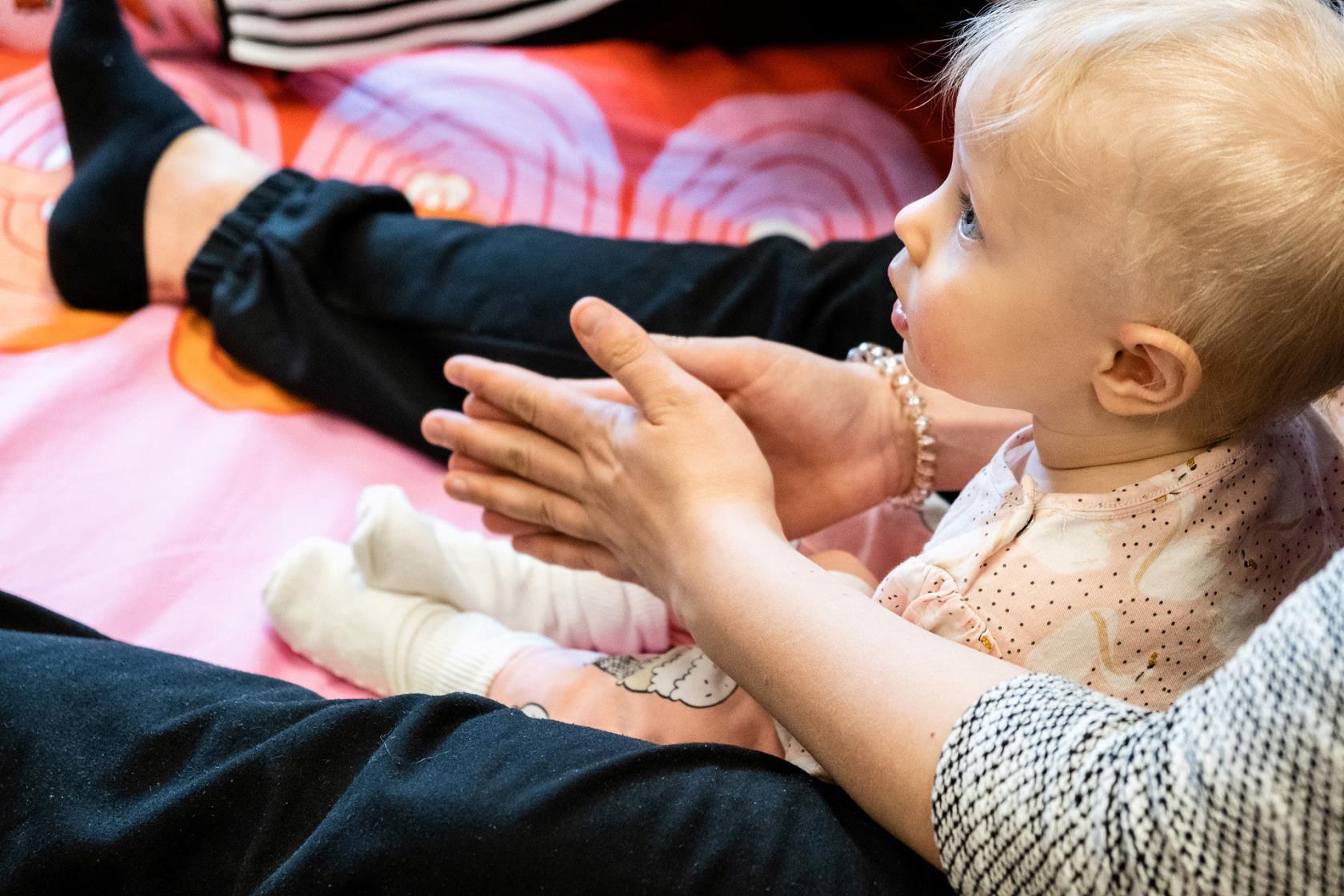 Bebissitter mellan vuxens ben. Vuxen klappar händerna.