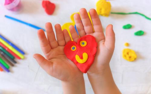 Barnhänder som håller i ett hempysslat lerhjärta.