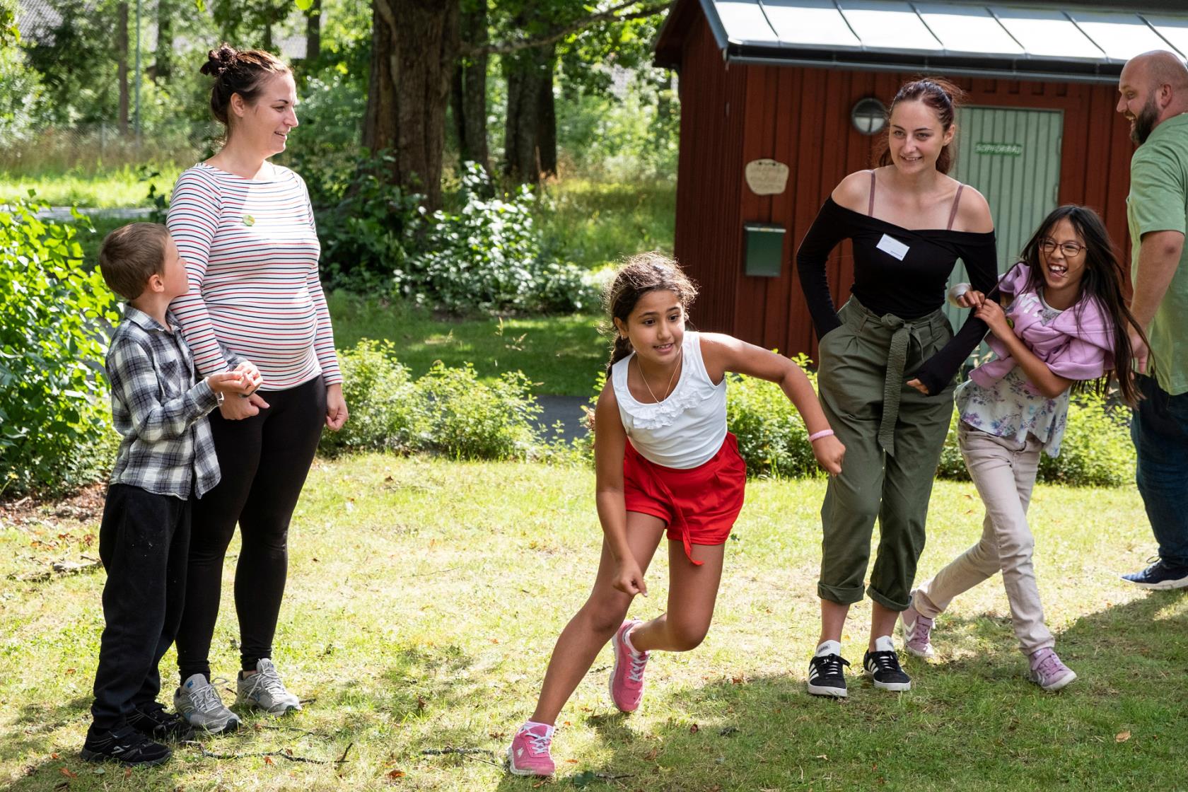 Vuxna och barn leker tillsammans utomhus på sommaren.