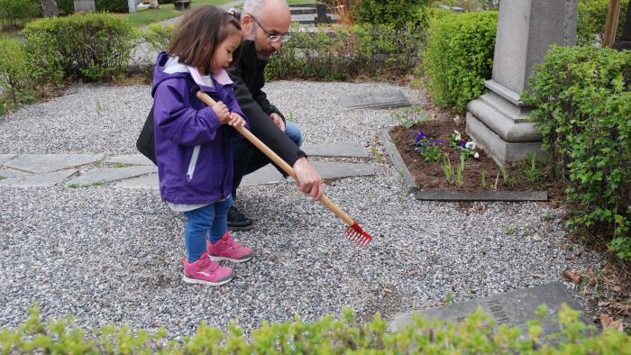 En pappa hjälper dotter att kratta gruset på en gravplats med en liten barnkratta.