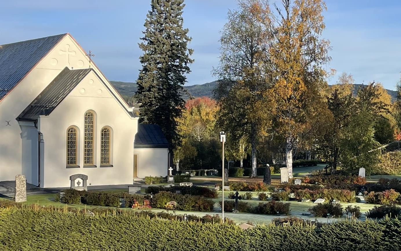 En bild av kyrka omgiven av frost belagda gräsytor och höstfärgade träd.