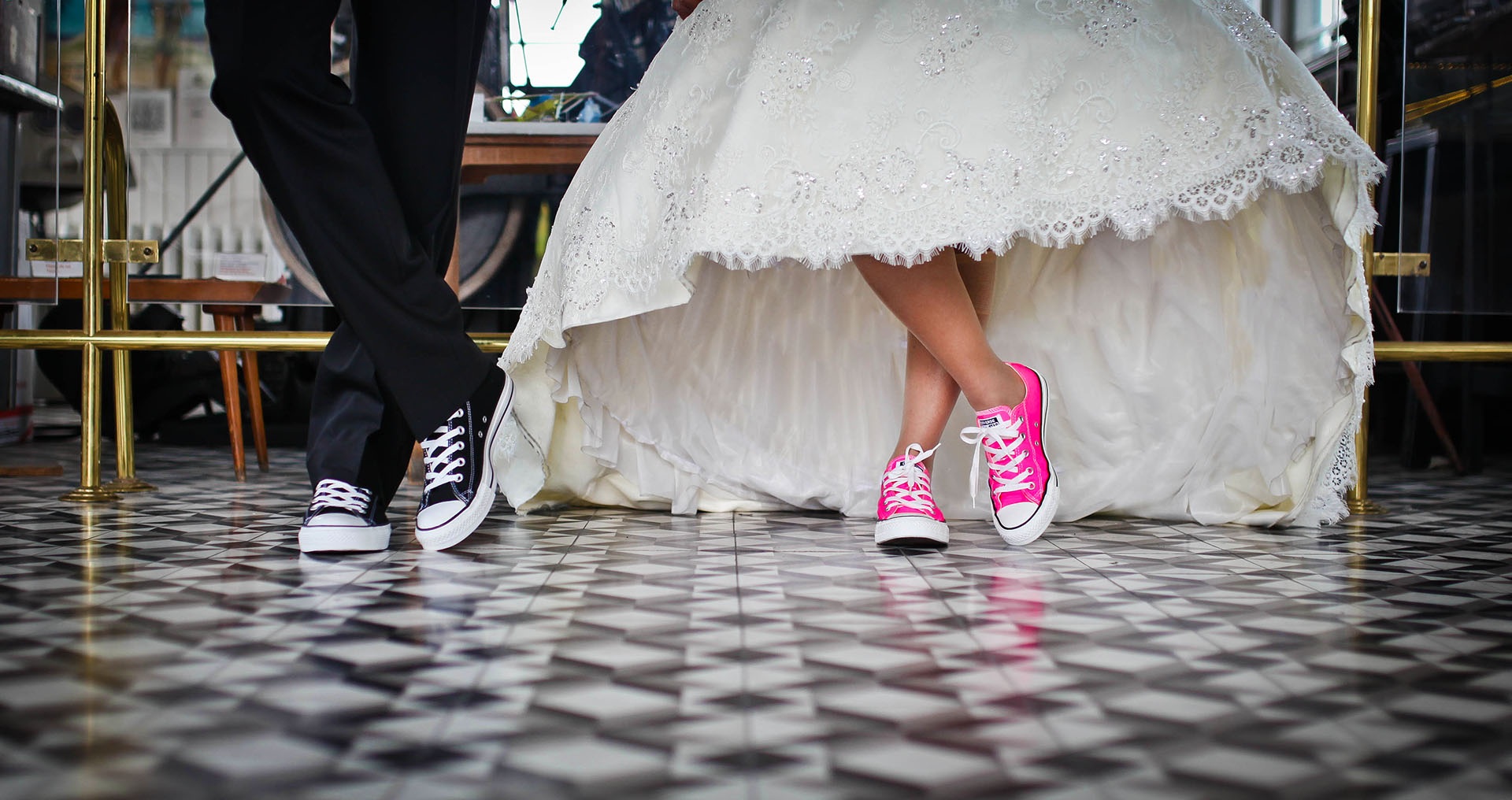 Ett brudpar fotograferat från knäna och nedåt. Vi ser klänning och kostymbyxor. På fötterna har de sneakers.