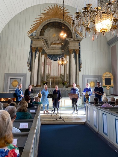 En kör på sju personer står längst fram i koret i en kyrka.